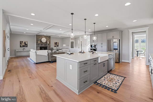 kitchen with gray cabinetry, a large fireplace, stainless steel appliances, light countertops, and light wood-type flooring