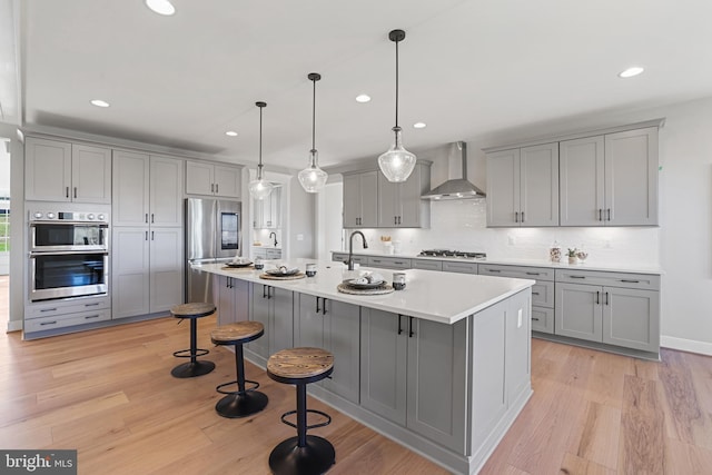 kitchen with appliances with stainless steel finishes, wall chimney range hood, and gray cabinetry