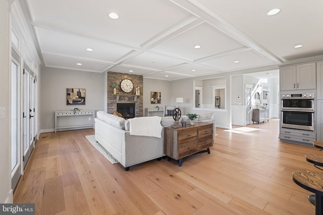 living room featuring light wood-style flooring, recessed lighting, coffered ceiling, and a stone fireplace