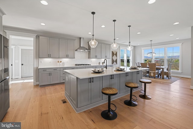 kitchen with light wood-style floors, wall chimney exhaust hood, stainless steel gas stovetop, and gray cabinets