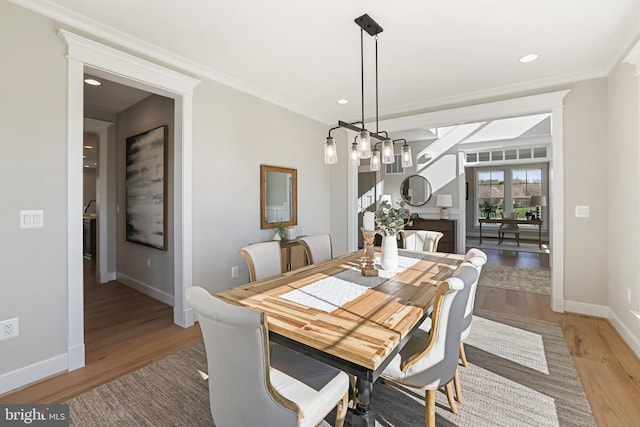 dining area featuring baseboards, light wood-style flooring, crown molding, a fireplace, and recessed lighting