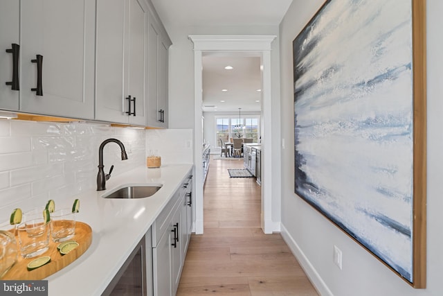 kitchen with gray cabinets, light countertops, backsplash, light wood-style flooring, and a sink