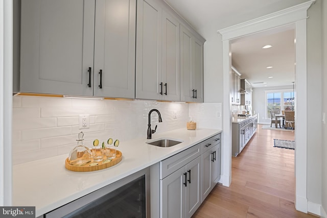 kitchen with light wood-style flooring, beverage cooler, a sink, light countertops, and backsplash