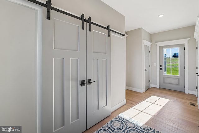 entryway featuring light wood finished floors, a barn door, visible vents, and baseboards