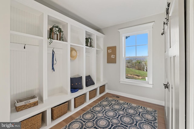 mudroom featuring visible vents, baseboards, wood finished floors, and a barn door