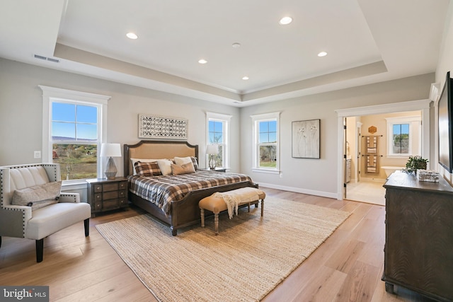 bedroom featuring light wood-style floors, visible vents, and a tray ceiling