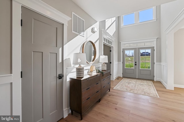 foyer featuring a wainscoted wall, french doors, light wood-style flooring, and visible vents