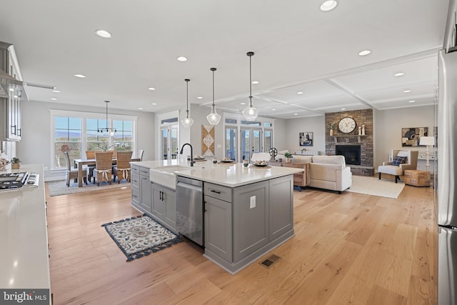 kitchen with gray cabinets, appliances with stainless steel finishes, light wood-style floors, a sink, and a stone fireplace