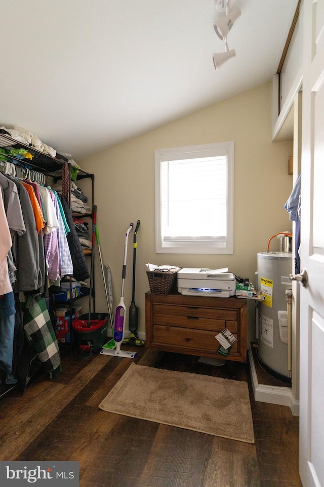 walk in closet with dark wood-type flooring, vaulted ceiling, and water heater