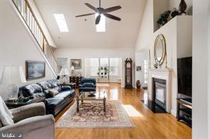 living room featuring a skylight, high vaulted ceiling, ceiling fan, and light wood-type flooring