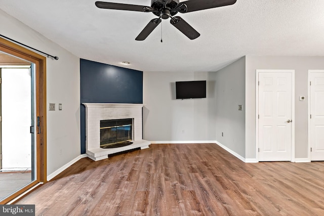 unfurnished living room featuring plenty of natural light, ceiling fan, a brick fireplace, and hardwood / wood-style flooring