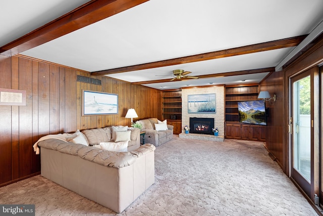 carpeted living room with a fireplace, wooden walls, built in features, ceiling fan, and beam ceiling