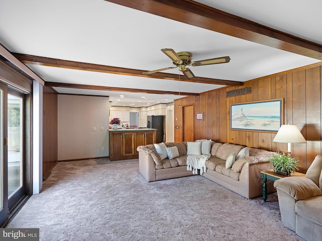 living room featuring wood walls, ceiling fan, beam ceiling, and light carpet