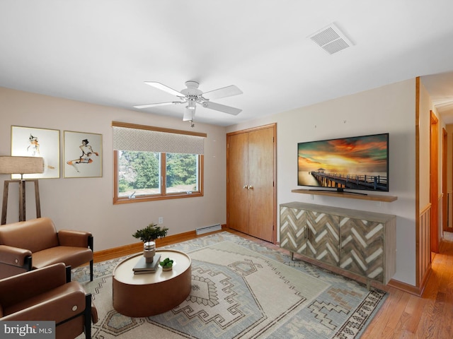 living room featuring baseboard heating, light hardwood / wood-style flooring, and ceiling fan