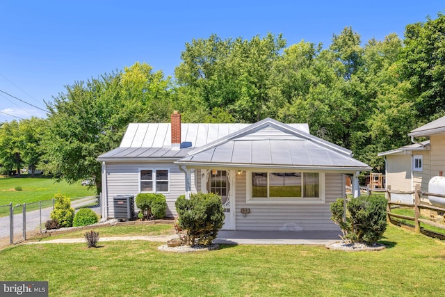 view of front of property with central AC, a front lawn, a standing seam roof, and fence