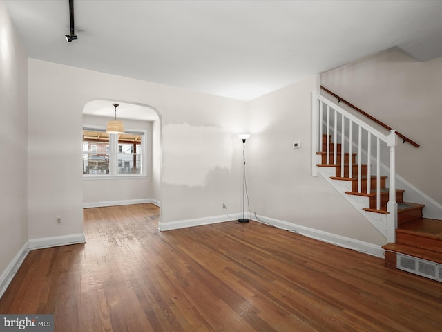 interior space featuring arched walkways, hardwood / wood-style flooring, visible vents, baseboards, and stairway