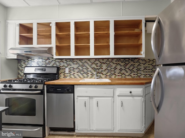 kitchen featuring butcher block counters, a sink, exhaust hood, appliances with stainless steel finishes, and tasteful backsplash