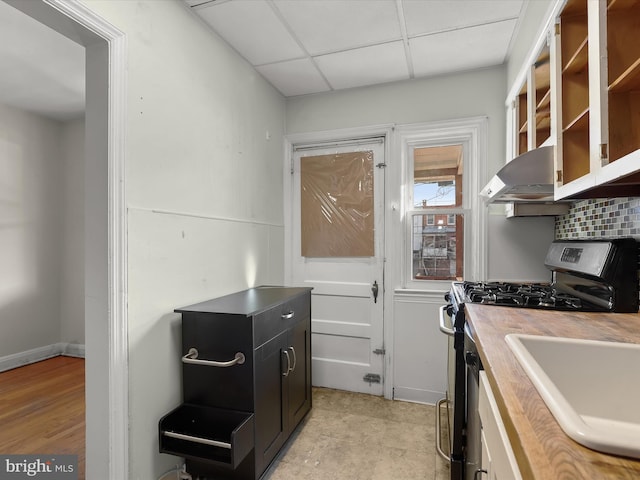 kitchen with a paneled ceiling, decorative backsplash, stainless steel gas stove, wall chimney range hood, and dark cabinets