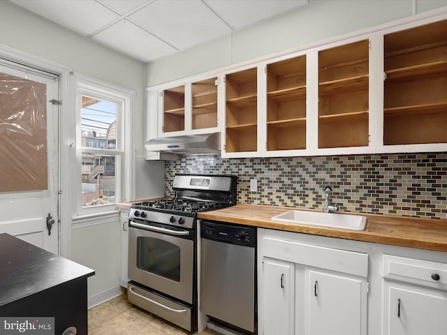 kitchen featuring butcher block counters, decorative backsplash, appliances with stainless steel finishes, a sink, and under cabinet range hood