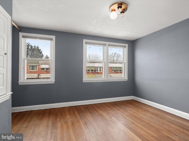 unfurnished room with wood-type flooring, a wealth of natural light, and baseboards