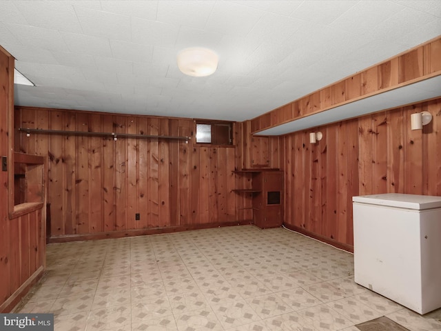 finished basement featuring baseboards, light floors, wooden walls, and refrigerator