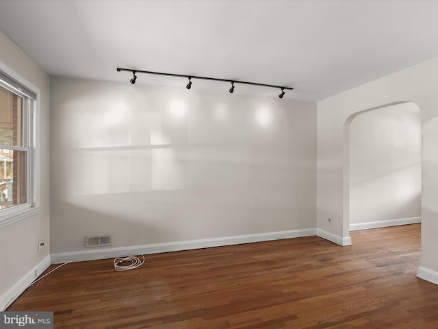 unfurnished room featuring arched walkways, wood finished floors, visible vents, and baseboards