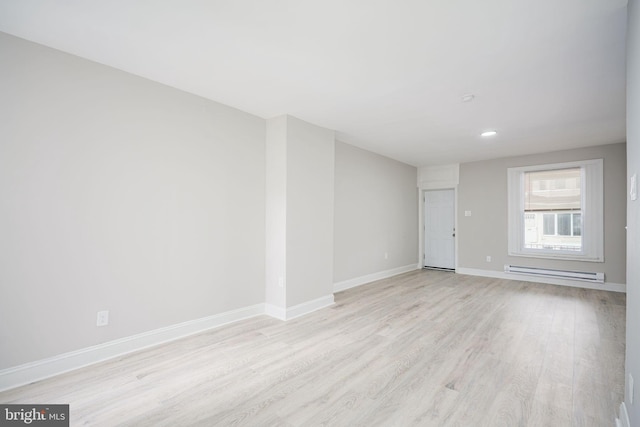 unfurnished room with a baseboard heating unit, baseboards, and light wood finished floors