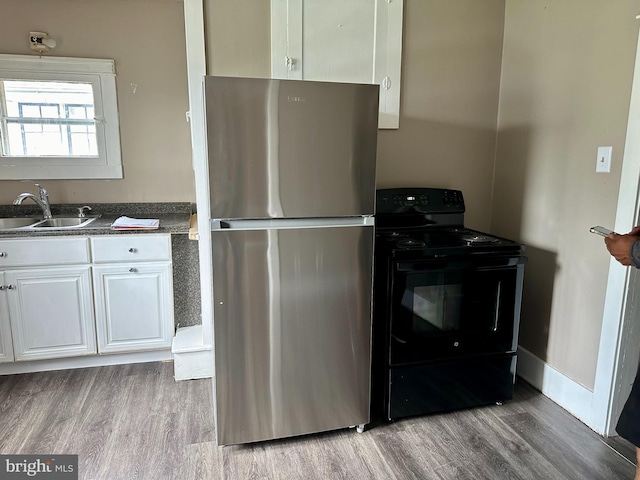 kitchen with black range with electric stovetop, stainless steel fridge, light hardwood / wood-style flooring, sink, and white cabinetry