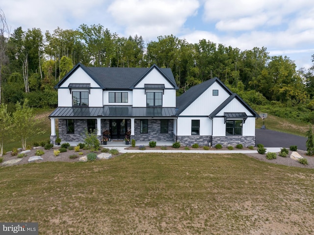 modern inspired farmhouse featuring metal roof, stone siding, a front lawn, and a standing seam roof