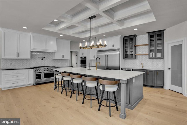 kitchen with premium appliances, beam ceiling, a breakfast bar area, and light wood finished floors