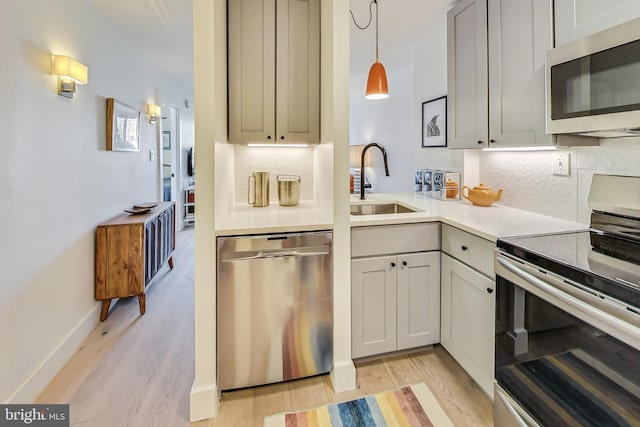 kitchen featuring light countertops, hanging light fixtures, decorative backsplash, appliances with stainless steel finishes, and a sink