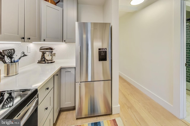 kitchen with baseboards, light wood-style floors, light countertops, stainless steel refrigerator with ice dispenser, and decorative backsplash