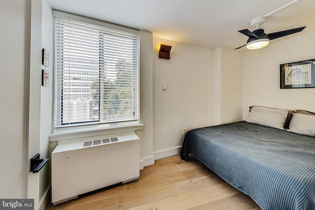 bedroom with radiator, light wood-style flooring, baseboards, and ceiling fan