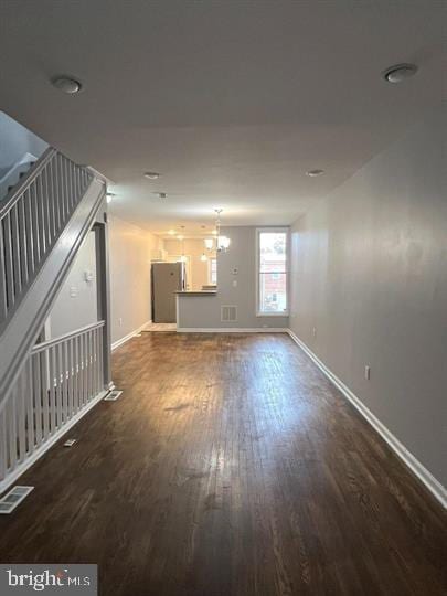 unfurnished living room featuring dark wood-type flooring, stairway, visible vents, and baseboards