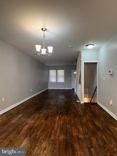 unfurnished living room with an inviting chandelier and dark hardwood / wood-style floors