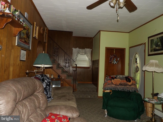 carpeted living room with ceiling fan, wood walls, and ornamental molding