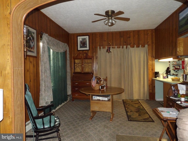 living area with ceiling fan, wooden walls, and carpet flooring