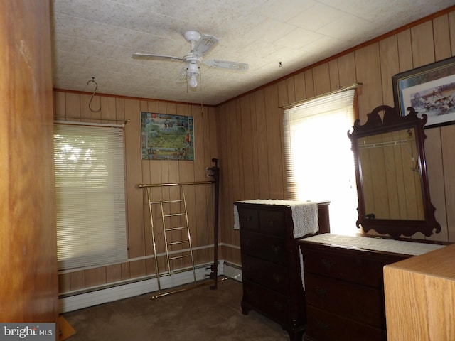 home office with dark colored carpet, ceiling fan, wood walls, and baseboard heating