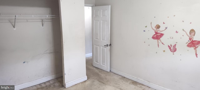 unfurnished bedroom with a closet, unfinished concrete flooring, and baseboards