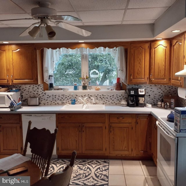 kitchen featuring light tile patterned flooring, backsplash, white appliances, a drop ceiling, and sink