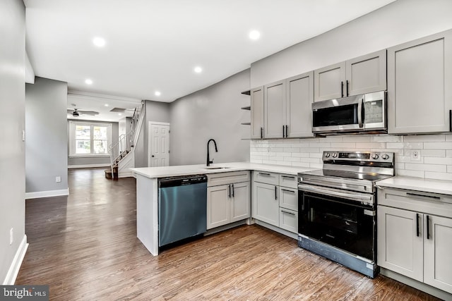 kitchen with open shelves, stainless steel appliances, light countertops, a sink, and a peninsula