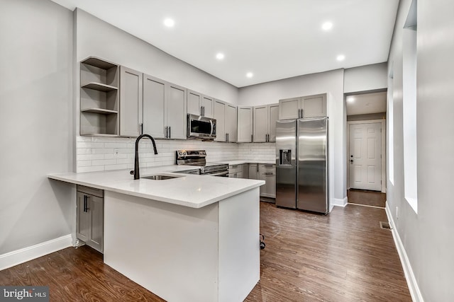 kitchen with sink, appliances with stainless steel finishes, dark wood-type flooring, and kitchen peninsula