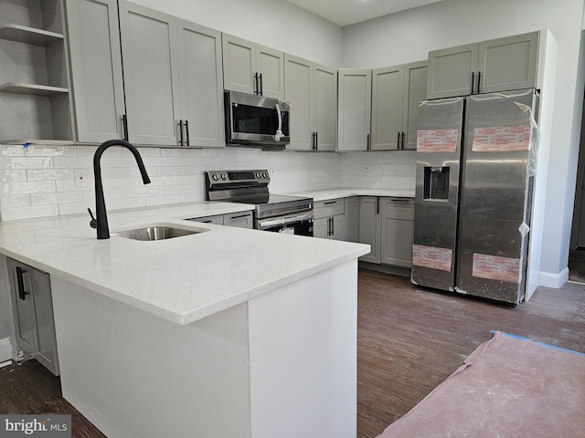 kitchen with appliances with stainless steel finishes, kitchen peninsula, sink, and dark hardwood / wood-style floors