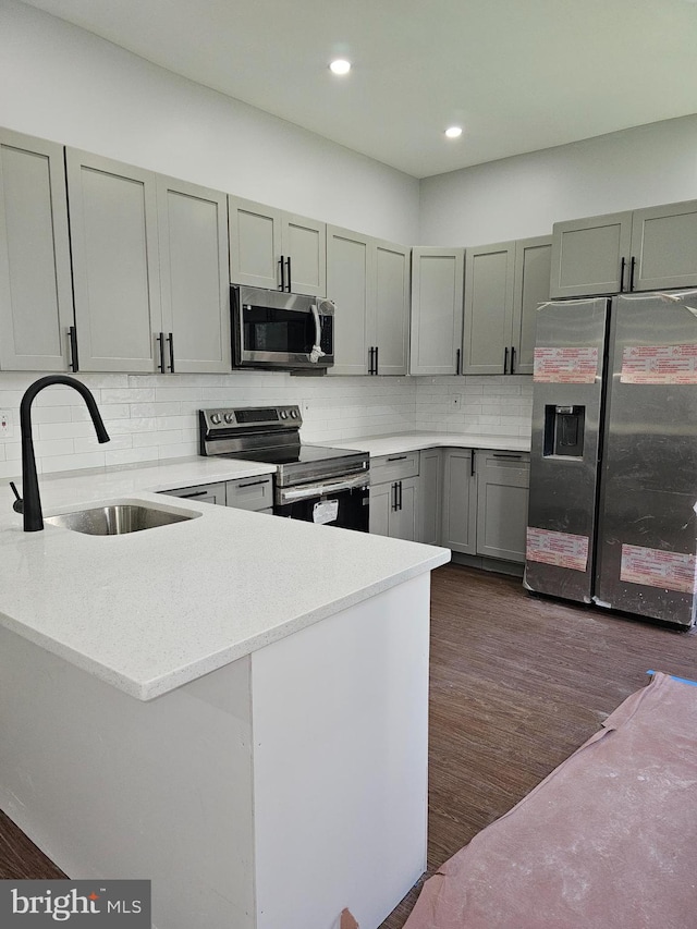 kitchen featuring dark hardwood / wood-style floors, tasteful backsplash, sink, kitchen peninsula, and appliances with stainless steel finishes