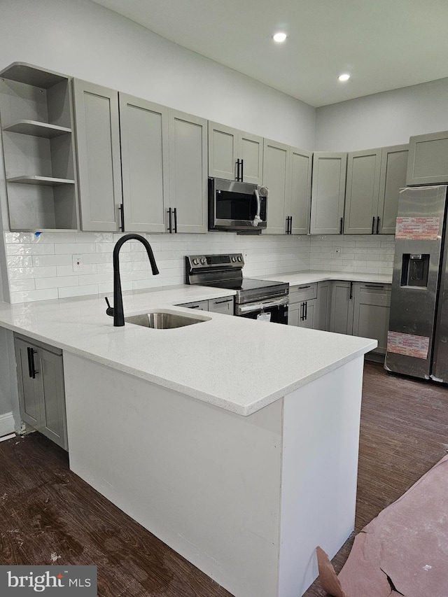 kitchen with tasteful backsplash, dark hardwood / wood-style flooring, sink, kitchen peninsula, and appliances with stainless steel finishes