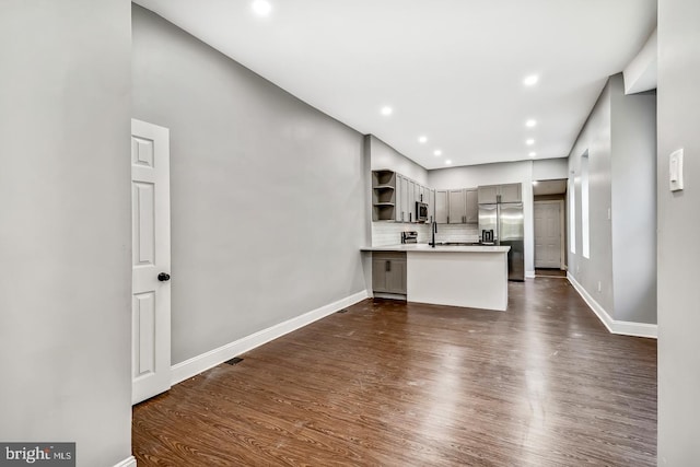 interior space with kitchen peninsula, dark wood-type flooring, stainless steel appliances, and backsplash