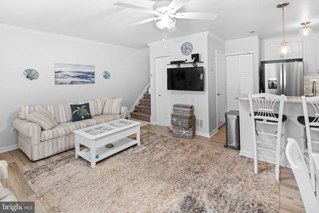 living room with ornamental molding, a ceiling fan, light wood-style floors, and stairs