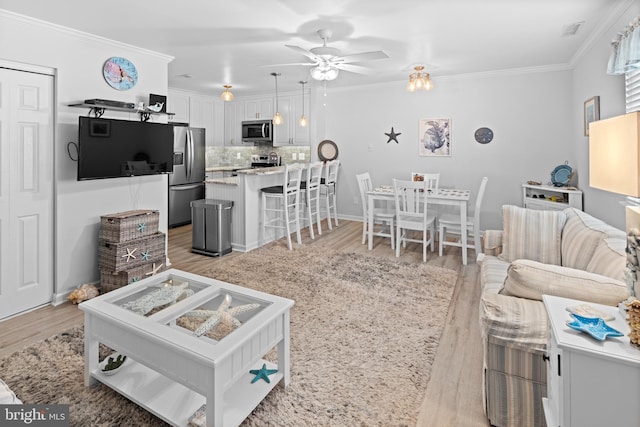 living area with ornamental molding, light wood-style floors, baseboards, and ceiling fan