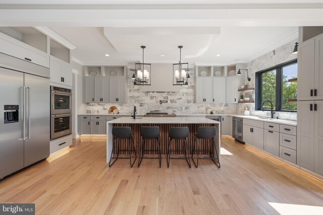 kitchen featuring stainless steel appliances, crown molding, an inviting chandelier, a center island with sink, and sink