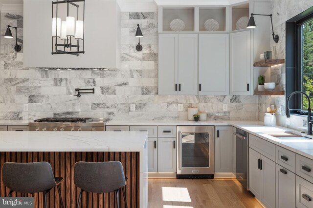 kitchen with white cabinets, wine cooler, hanging light fixtures, light hardwood / wood-style flooring, and light stone countertops